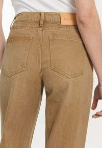 Bruine denim hoge taille broek met een gestructureerde afwerking, twee achterzakken en een leren label aan de taille.