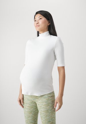 White fitted top with a high neck and short sleeves, paired with textured green patterned pants. The fabric appears smooth and stretchy.