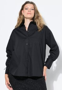 Camicia nera a maniche lunghe realizzata in tessuto morbido, con una tasca sul petto e una vestibilità comoda.
