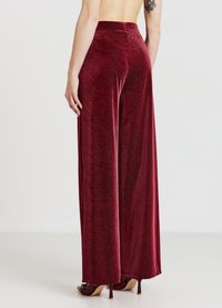 Hose mit weitem Bein aus strukturiertem, weichem rotem Stoff mit einem dezenten Muster. Hoher Bund, bodenlang, kombiniert mit hochhackigen Schuhen.