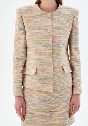 Giacca beige textured con strisce orizzontali colorate, bottoni rotondi e una forma leggermente strutturata. Presenta due tasche frontali e maniche lunghe.