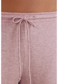 Ribbade, ljusrosa loungebyxor med dragsko i midjan. Närbild visar textur och sömdetaljer på midjebandet och snöret.