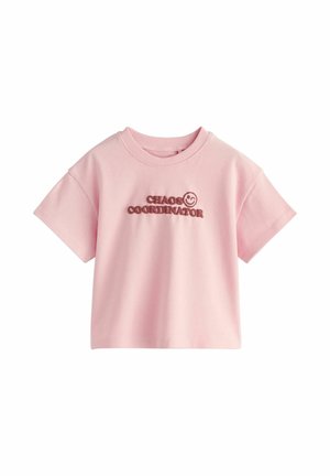 Lyserød kortærmet cropped T-shirt med teksten "CHAOS COORDINATOR" og et smilende ansigt trykt i mørk pink på brystet.