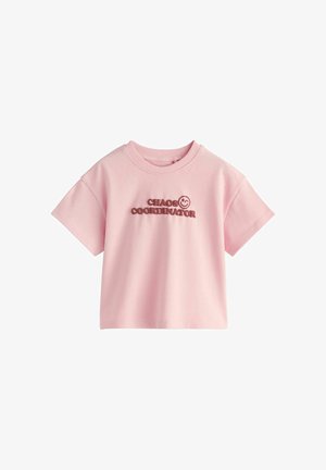 Lyserød kortærmet cropped T-shirt med teksten "CHAOS COORDINATOR" og et smilende ansigt trykt i mørk pink på brystet.