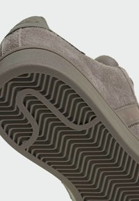 Baskets en daim gris présentant une semelle en caoutchouc avec un motif ondulé texturé, dotées d'un logo subtil sur la languette et d'éléments de design minimalistes.