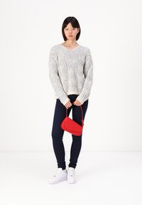 Lichtgrijze kabelgebreide sweater met een diepe V-hals, marineblauwe leggings en een kleine rode handtas. Witte sneakers maken de outfit compleet.