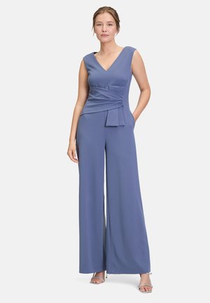Combinaison à décolleté en V en tissu bleu doux, avec un corsage ajusté, un détail de taille froncée, des jambes larges et des poches latérales discrètes.