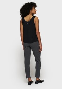 Zwarte mouwloze tanktop, grijze joggers en zwarte instappers. Focus op eenvoudige lijnen, zachte stof en een relaxte pasvorm.