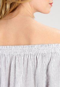 Hübsches Off-Shoulder-Oberteil mit weißen und schwarzen vertikalen Streifen, ausgestattet mit einem gerafften elastischen Ausschnitt und einem fließenden Stofftextur.
