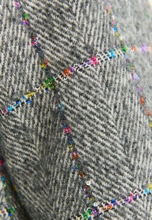 Zbliżenie na szary materiał w jodełkę z kolorowymi koralikami i cekinami wzdłuż wyszywanych wzorów diamentowych.