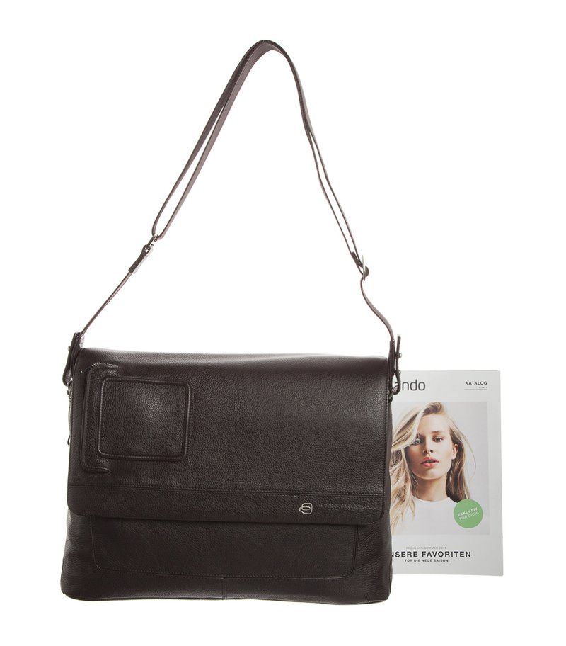 Borsa a tracolla in pelle marrone con pattina, tracolla regolabile, superficie testurizzata, tasca frontale e una rivista parzialmente visibile accanto ad essa.