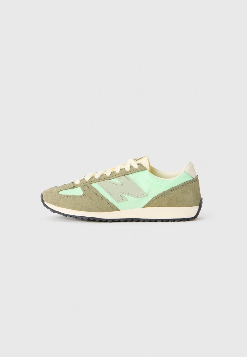 Baskets basses en daim vert olive avec des panneaux en tissu vert menthe, lacets crème clair et semelle noire rainurée sur fond gris.