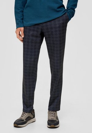 Donker geruite broek van een gestructureerde stof. De pasvorm is recht, en ze zijn gecombineerd met beige en marineblauwe sportschoenen.