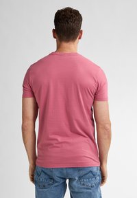 T-shirt a maniche corte di colore rosa pallido, realizzato in morbido cotone, con scollatura rotonda e una vestibilità rilassata, visto da dietro.
