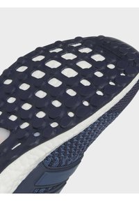 Semelle en caoutchouc texturée bleu foncé avec motifs circulaires d’adhérence sur une semelle intermédiaire blanche et tige de chaussure en maille bleu marine.