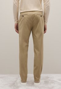 Pantalones caquis hechos de tejido suave. Cuentan con dos bolsillos traseros con botones y un diseño de pierna ajustada, combinados con zapatillas blancas.