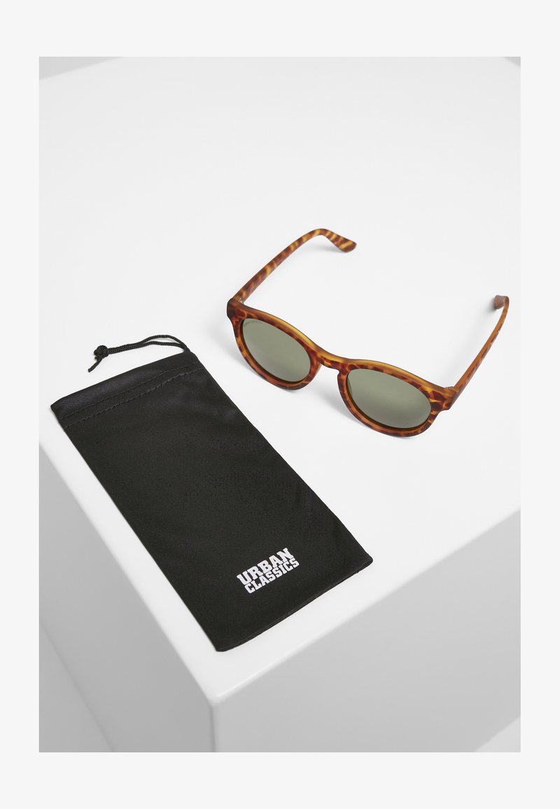 Ochelari de soare din fibră de țesătură cu lentile verzi, având rame rotunde. Însoțiți de un sac cu șnur negru, cu logo-ul "URBAN CLASSICS".