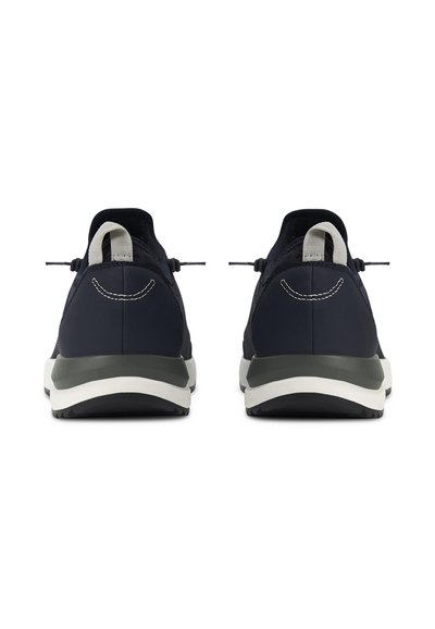 Une paire de baskets basses noires vue de l'arrière avec des semelles blanches et grises et des tirettes sur les talons, sur fond blanc.