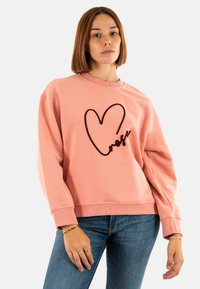 Sudadera rosa hecha de una tela suave, con un corte holgado, escote redondeado y un diseño de corazón bordado en negro.