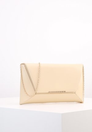 Pochette enveloppe rectangulaire beige avec chaîne dorée et petite plaque métallique à l’avant, posée sur un socle blanc.