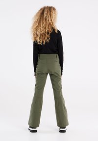 Pantaloni da sci altezza vita in verde oliva, con gambe larghe e svasate, dotati di tasche posteriori e una finitura liscia e texture. Visibile un top nero a maniche lunghe.