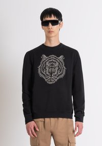 Felpa nera con una grafica dettagliata di una tigre color crema. Realizzata in tessuto morbido, presenta un colletto a girocollo e maniche lunghe.