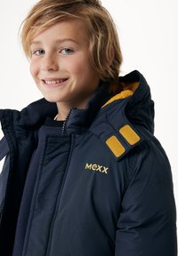 Marinblå pufferjacka med gula accenter på axlarna, har en hög krage, dragkedjestängning och broderad logotyp på bröstet.