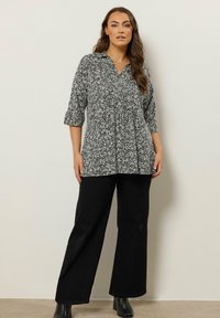 Blusa a righe bianco e nero con colletto, maniche a tre quarti e design davanti a pieghe; abbinata a pantaloni neri a gamba larga e stivaletti.