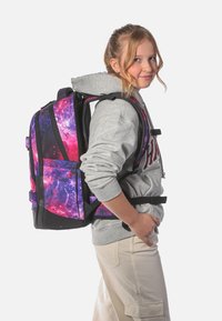 Batoh s galaxiovým vzorem má fialové a růžové vzory s černými akcenty. Nastavitelné popruhy a více přihrádek pro úložný prostor.