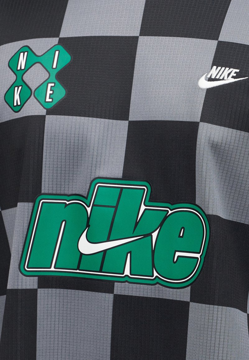 Schwarz-grau kariertes Stoff mit drei grünen und weißen Nike-Logos, einem großen in der Mitte und zwei kleineren oben an den Seiten.