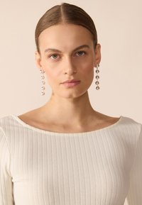 Silver drop earrings with round beads, featuring a line of alternating sizes. Worn with a ribbed white top, showcasing a wide neckline.