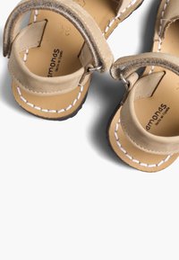 Beige nahkakengät vauvoille valkoisella ompelulla, nilkkaremmillä ja brändinimi "Pamonas" painettuna vaalean ruskeille pohjille.