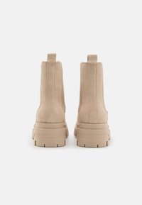 Beige Wildleder-Ankle Boots mit einer stabilen Gummisohle, die über vertikale Nähte und Anzieh-Schlaufen an der Rückseite für einfaches An- und Ausziehen verfügen.