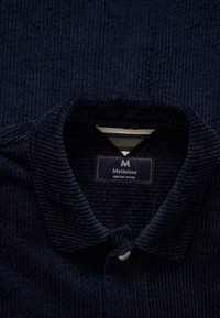Donkerblauwe geribbelde corduroy overhemdkraag met een zichtbaar Matinique Heritage Apparel label aan de binnenkant.