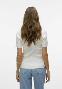 Geribbeld wit T-shirt met korte mouwen en een getailleerd ontwerp, gecombineerd met lichtblauwe high-waisted jeans. Soepele textuur met subtiele details bij de naden.