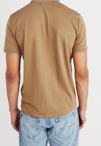 Kaki bomullspiké med korta ärmar, ribbad krage och texturerade muddar, matchad med ljusblå denimjeans. Bakifrån visad.