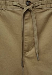 Un pantalon en coton kaki avec une taille à cordon, une fermeture par bouton et une poche latérale. Le tissu est lisse avec un léger éclat.