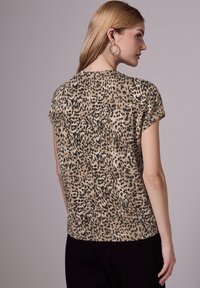 Top de estampado de leopardo en beige y negro, con mangas cortas, corte relajado y textura suave. La parte posterior presenta una costura central para un detalle adicional.