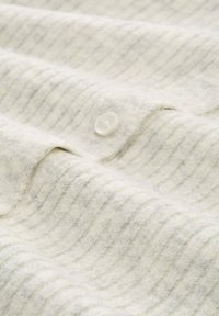 Țesătură moale, cu un model ribat, de culoare crem, cu un buton mic alb cosut aproape de o detaliu de cusătură pliat.
