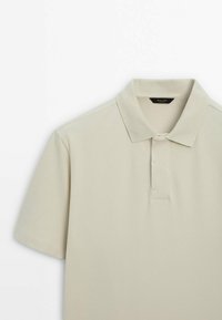 Polo manches courtes beige clair avec col classique et patte de boutonnage partielle, présenté sur un fond blanc.