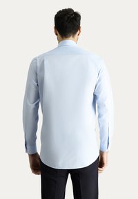 Camicia azzurra a maniche lunghe con taglio dritto, polsini a bottone e una texture di tessuto liscia, mostrata dal retro contro uno sfondo neutro.