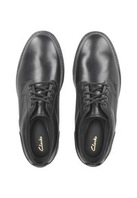 Chaussures en cuir noir avec une finition lisse, dotées de bouts ronds, de six œillets et d'une semelle intérieure rembourrée avec la marque "Clarks".