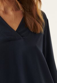 Haut bleu marine avec un design en V, présentant une texture douce et des manches longues. Le tissu semble lisse et tombe doucement.