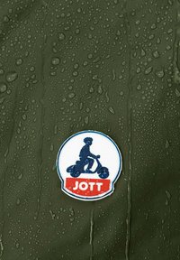 Tessuto verde scuro idrorepellente con gocce d'acqua, con un logo circolare raffigurante un bambino su uno scooter, etichettato "JOTT" in rosso.