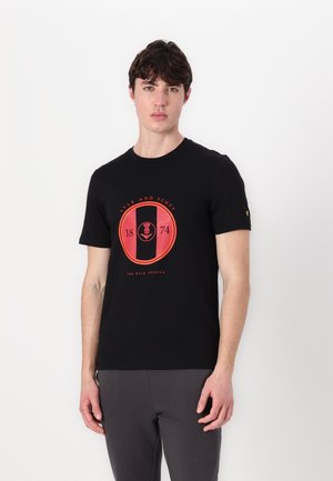 Juoda medvilnė marškinėliai su apvalia raudona ir juoda grafika, kurioje yra tekstai "Lyle and Scott", "1874" ir "The Wild Thistle". Trumpomis rankovėmis.