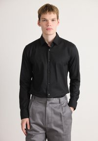 Zwarte longsleeve shirt met een button-down kraag, voorzien van bijpassende knopen en gladde stof, gecombineerd met lichtgrijze geplooide broek.