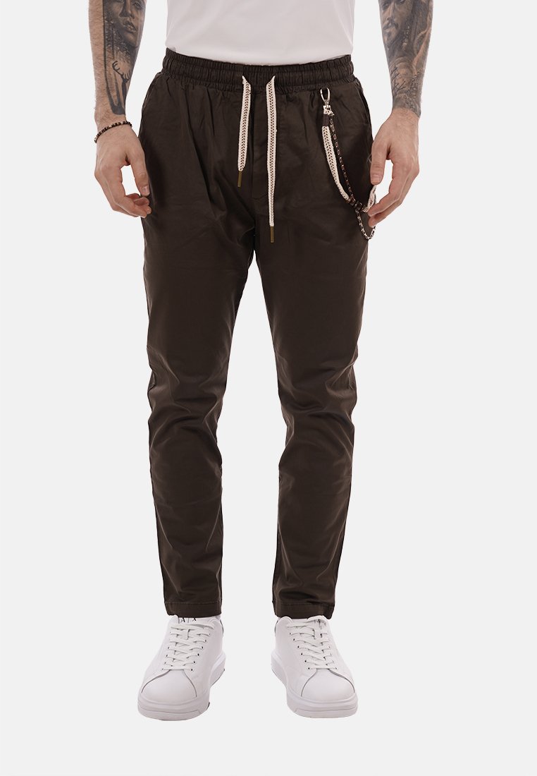 Uomo che indossa pantaloni jogger neri con coulisse bianche e un portachiavi, abbinati a scarpe da ginnastica bianche e braccia tatuate.