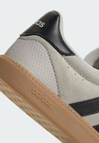 Smeđa tenisica od brušene kože s crnim kožnim detaljima, s teksturiranim gornjim dijelom, gumom tabanom i utisnutim adidas logotipom sa strane.