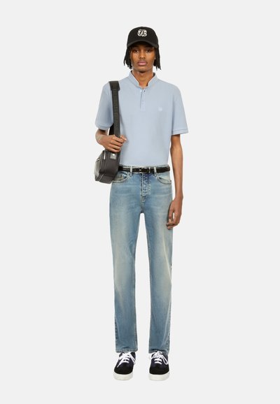 Polo shirt azzurro chiaro con maniche corte, jeans chiari, scarpe da ginnastica nere e un cappellino nero. Il modelloporta una piccola borsa a tracolla nera.