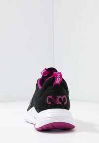 Scarpa sportiva nera e viola con suola bianca, con il numero "23" e il testo "JRDN" in viola sul tallone, fotografata da dietro su una superficie bianca.